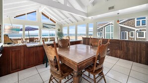 A spacious kitchen with a large island, wooden chairs, and a view of the beach.