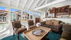 A spacious living room with a high ceiling, large windows, and a view of neighboring houses.