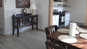 A dining area with a wooden table, chairs, and a ceiling fan. There is a kitchen visible through an open doorway. - Twin Nest Duplex (Irving)