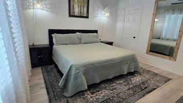 A bedroom with a bed, a ceiling fan, a wall-mounted light, a door, and a mirror.