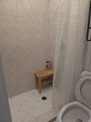 Une petite salle de bain avec une douche, des toilettes et un banc en bois.