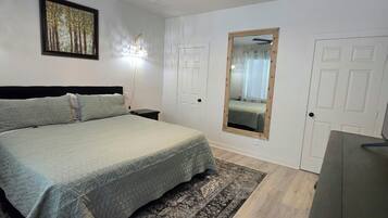 A bedroom with a bed, a ceiling fan, a mirror, and a door.
