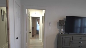 A hallway with a TV on a dresser, a patterned rug, and a door leading to another room. - Twin Nest Duplex (Irving)