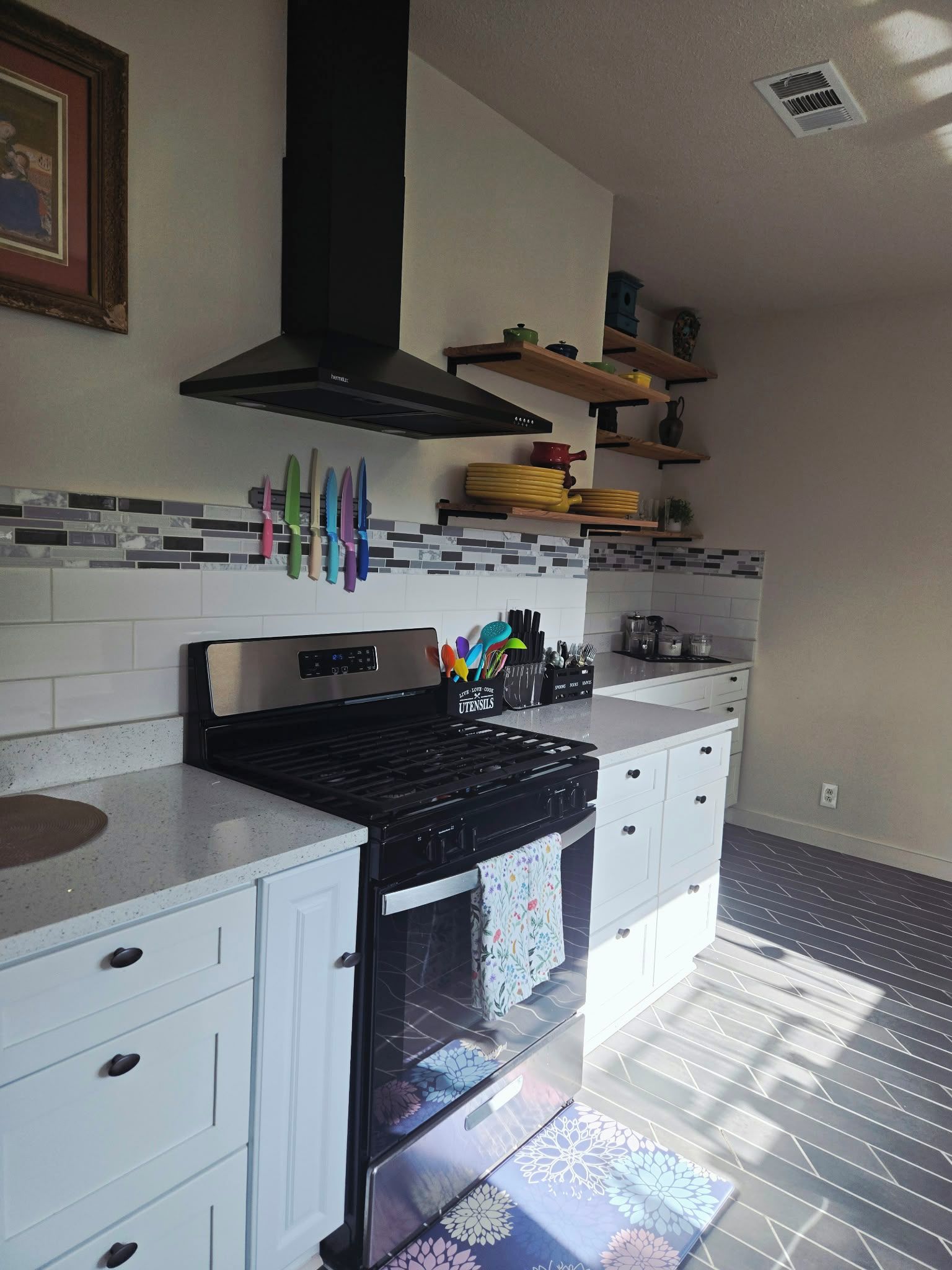 A kitchen with a black range hood, white cabinets, and a tiled backsplash.