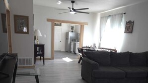A living room with a sofa, a coffee table, a dining table, and a kitchen in the background. - Twin Nest Duplex (Irving)
