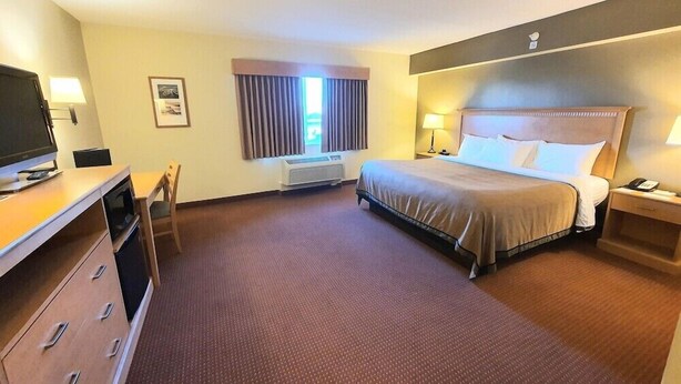 Ett hotellrum med en säng, ett skrivbord med en tv, en stol, en lampa och ett fönster med gardiner.