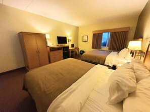 Ein Hotelzimmer mit zwei Betten, einem Schreibtisch mit Computer, einem Kleiderschrank und einem Fenster mit Vorhängen.