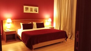 A hotel room with a large bed, two bedside tables with lamps, a red carpet, and a framed picture on the wall. - Barragem DA Aguieira (Mortagua)