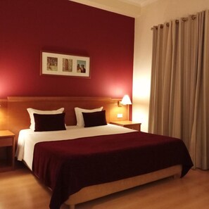 A hotel room with a bed, a nightstand, a lamp, a wall-mounted picture, and a curtain. - Barragem DA Aguieira (Mortagua)