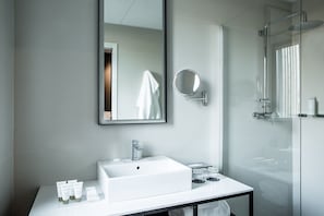 A modern bathroom with a large mirror, a sink, and a glass shower enclosure. - Hotel Louvre Lens (Lens)