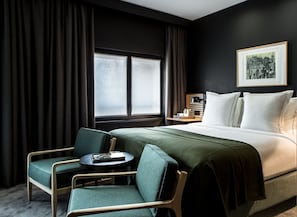 A hotel room with a bed, two chairs, a small table, a nightstand with a kettle, and a framed picture on the wall. - Hotel Louvre Lens (Lens)