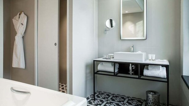 A modern bathroom with a white sink, a mirror, and a towel rack. - Hotel Louvre Lens (Lens)