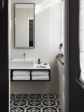 A bathroom with a white sink, a mirror, and a black and white patterned floor. - Hotel Louvre Lens (Lens)