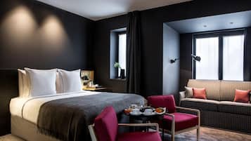 Une chambre d’hôtel moderne dotée d’un grand lit, d’un canapé, d’une table à manger où le petit-déjeuner est servi, et offrant une vue sur la ville.