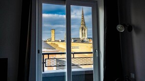A view from a balcony with a glass door, overlooking a cityscape with a prominent cathedral spire and a tower. - Alive Hotel de Quebec (Rouen)