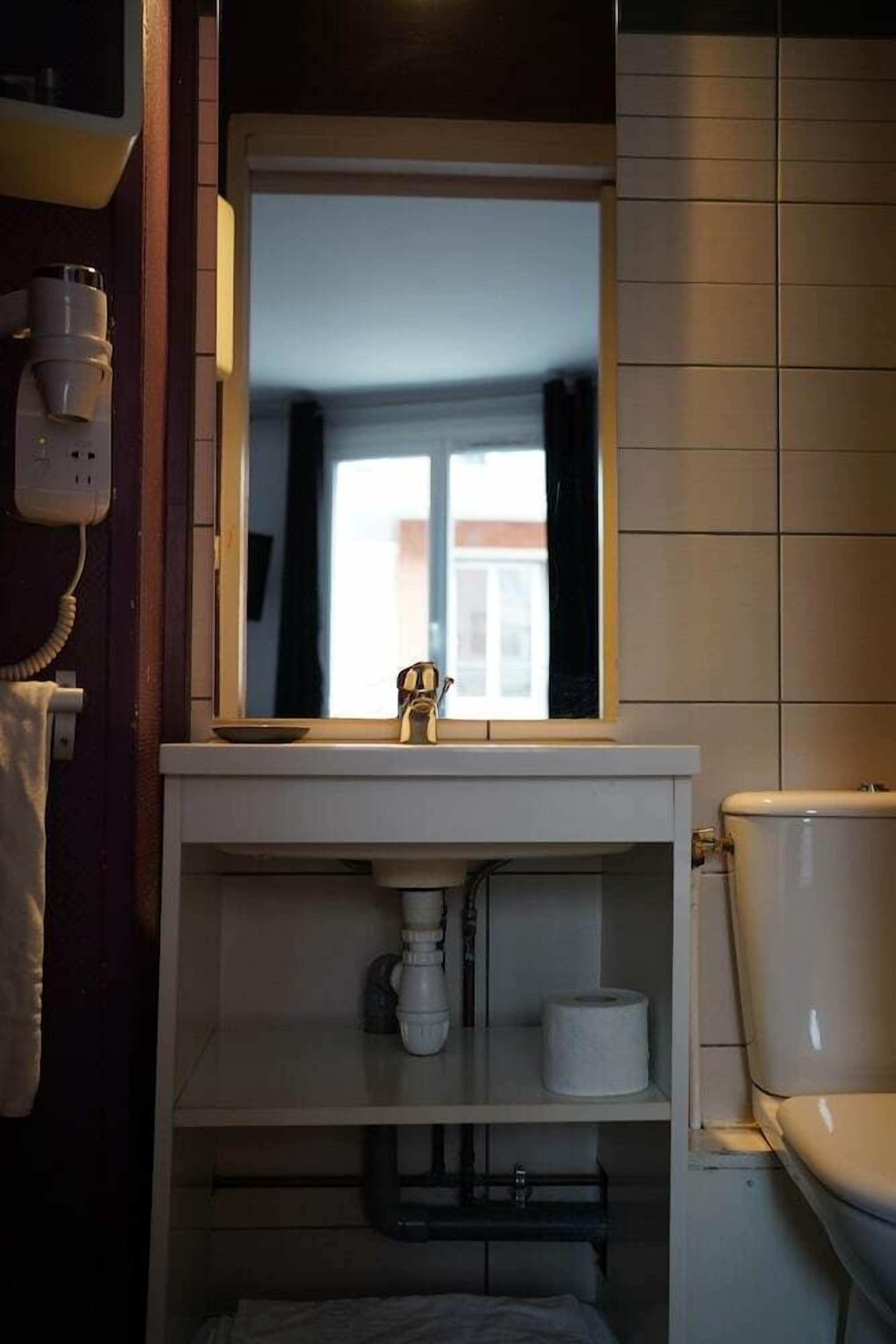 Een badkamer met een wit wastafel, een spiegel erboven, een toilet en een raam.
