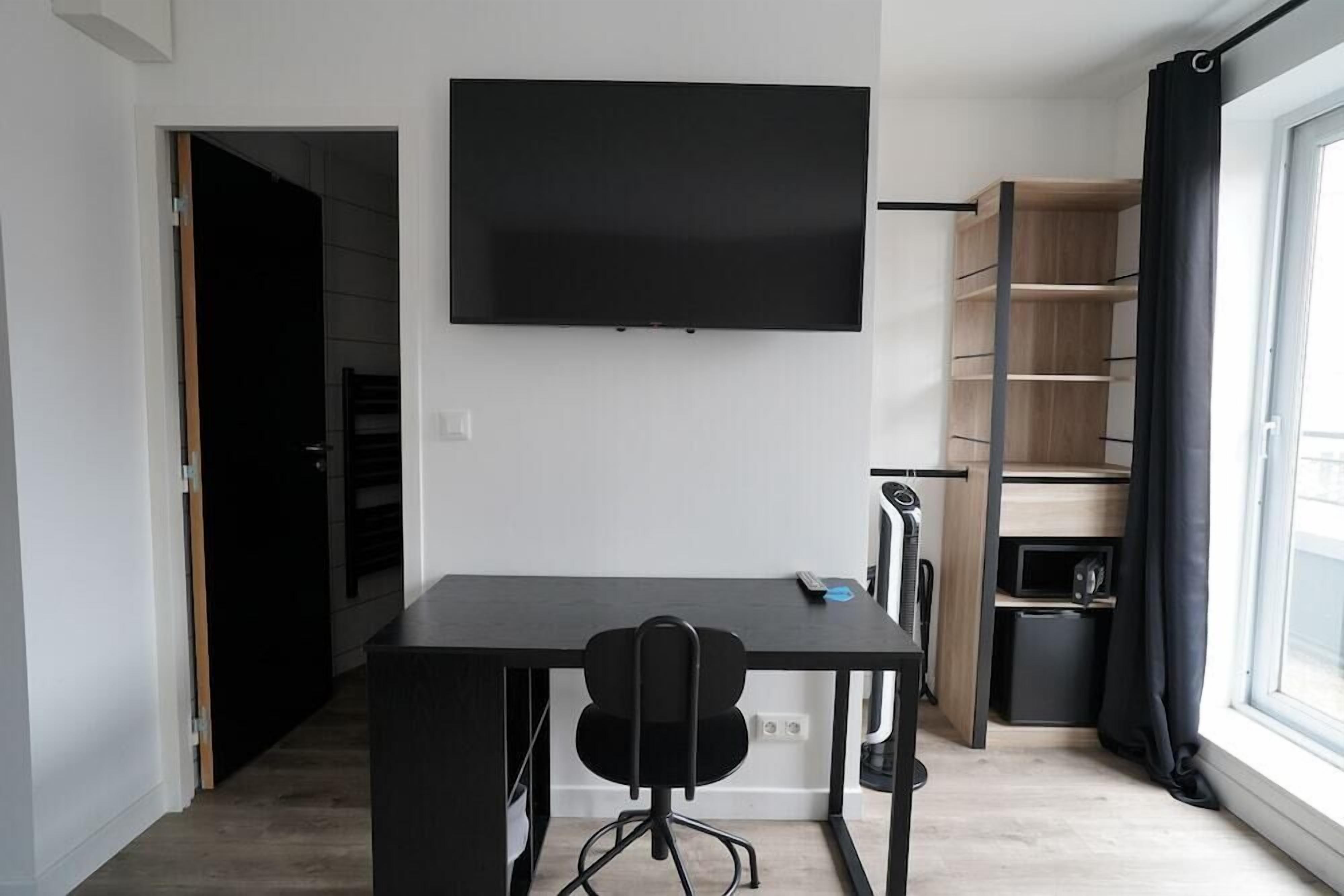 Un espacio moderno para vivir con un televisor de pantalla plana montado en la pared, un escritorio negro con una silla y una estantería empotrada con puerta corredera.