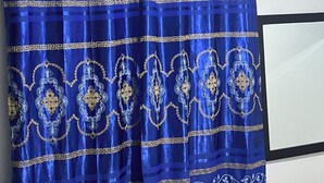 Un rideau bleu orné de motifs dorés et blancs, un mur blanc et un appareil de climatisation blanc.