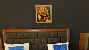 Un lit bien fait, avec un matelas blanc et deux oreillers bleus, une tête de lit en bois et un tableau encadré accroché au mur.