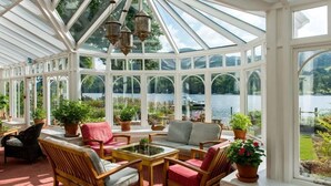 Un invernadero con techo de cristal, muebles de madera y plantas en macetas.