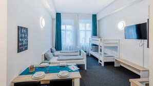 A hotel room with bunk beds, a dining table set with plates and glasses, a TV mounted on the wall, and a window with curtains. - Centerroom Landshut City (Landshut)