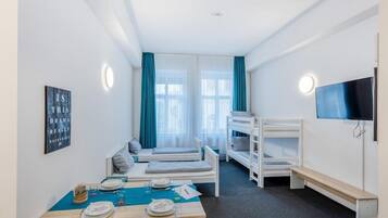 Ein Hotelzimmer mit Stockbetten, einem Esstisch gedeckt mit Tellern und Gläsern, einem an der Wand montierten Fernseher und einem Fenster mit Vorhängen.