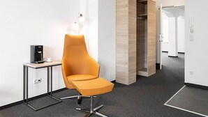 A modern hotel lobby with a high chair, a coffee machine, and a wooden accent wall. - Centerroom Landshut City (Landshut)