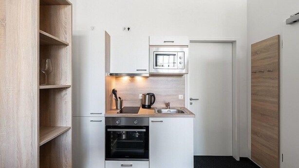 A compact kitchen with white cabinetry, a built-in oven, a microwave, and a coffee maker. - Centerroom Landshut City (Landshut)