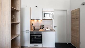 Eine kleine Küche mit weißen Schränken, einem eingebauten Backofen, einer Mikrowelle und einer Kaffeemaschine.