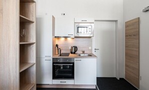 A compact kitchen with white cabinetry, a built-in oven, a microwave, and a coffee maker. - Centerroom Landshut City (Landshut)
