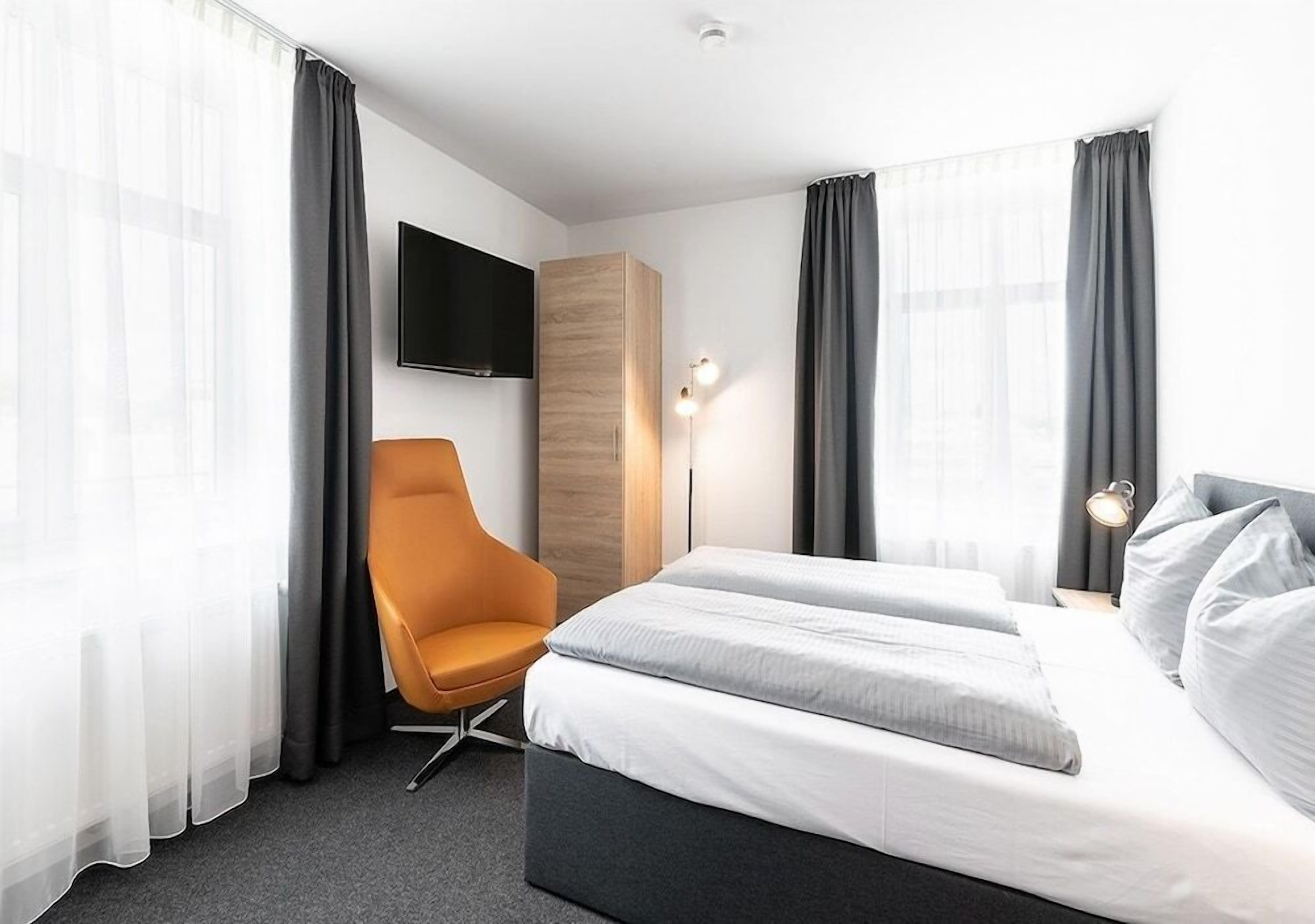 A hotel room with a bed, a chair, a TV, and a lamp.