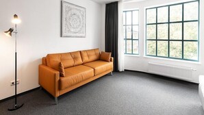 A modern room with a sofa, a floor lamp, a large window, and a radiator. - Centerroom Landshut City (Landshut)