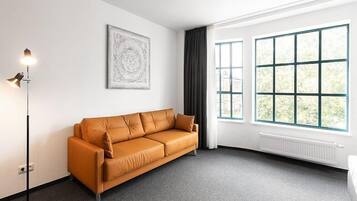 Ein modernes Zimmer mit einer Couch, einer Stehlampe, einem großen Fenster und einer Heizung.