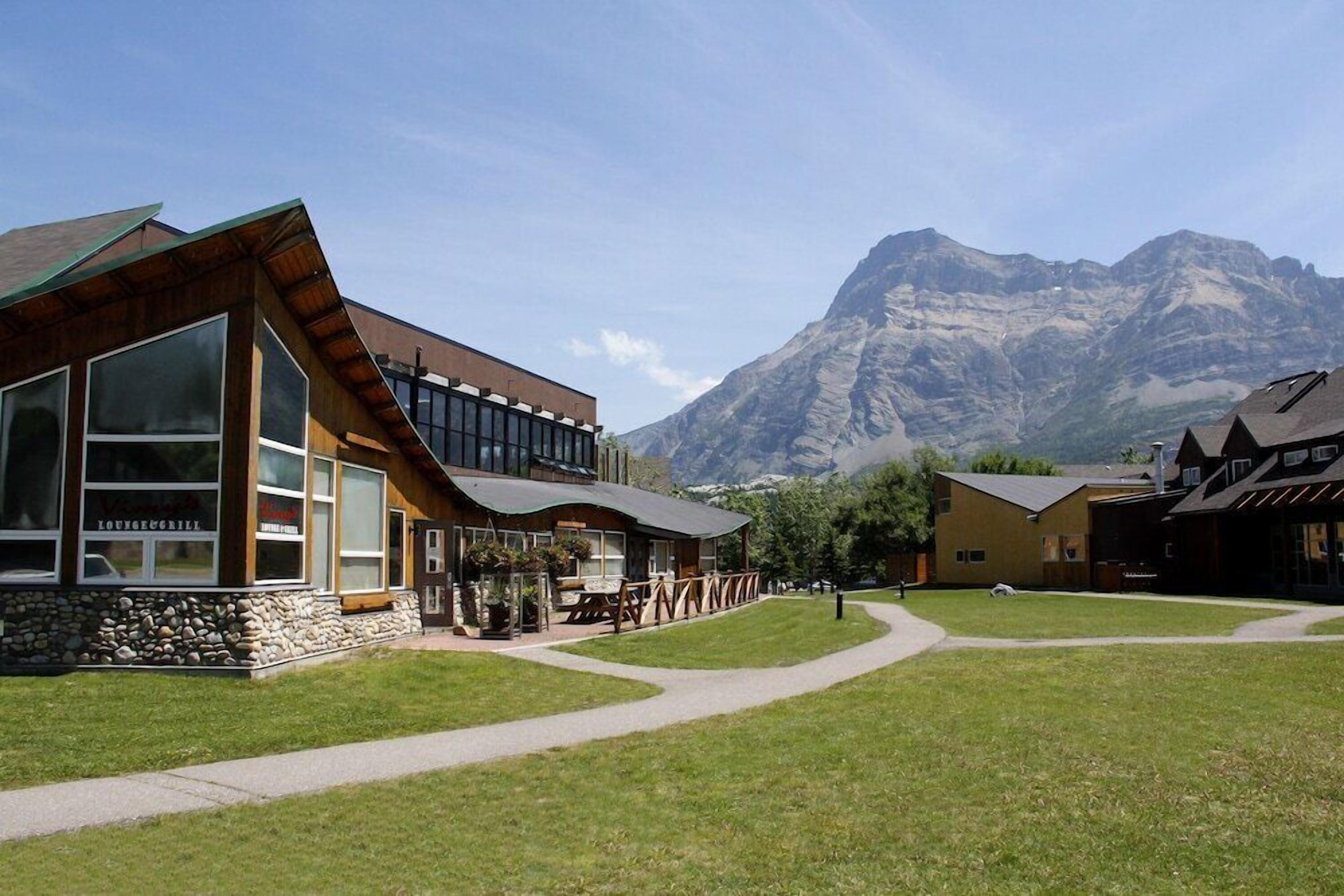 A lodge with large windows, a stone facade, and a mountain backdrop.