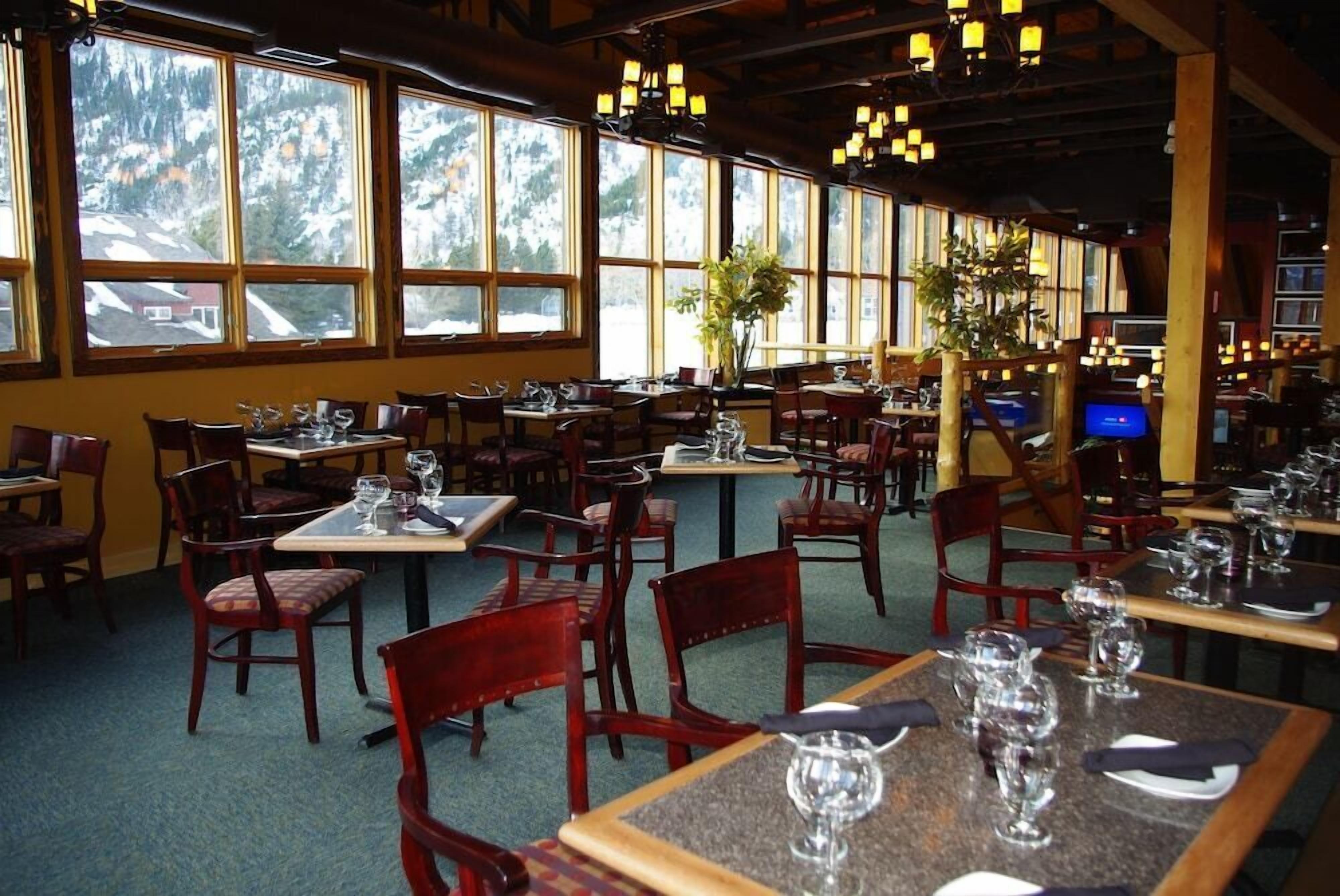 A restaurant with multiple tables and chairs, large windows with a view of snow-capped mountains, and hanging lantern-style lights.
