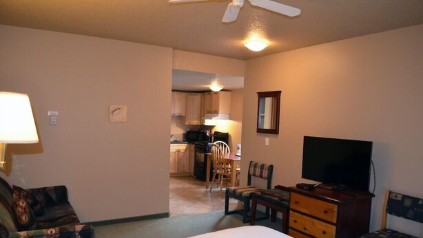 A hotel room with a bed, a TV, a dresser, and a chair. There is a kitchenette in the background. - Waterton Lakes Lodge Resort (Waterton Park)