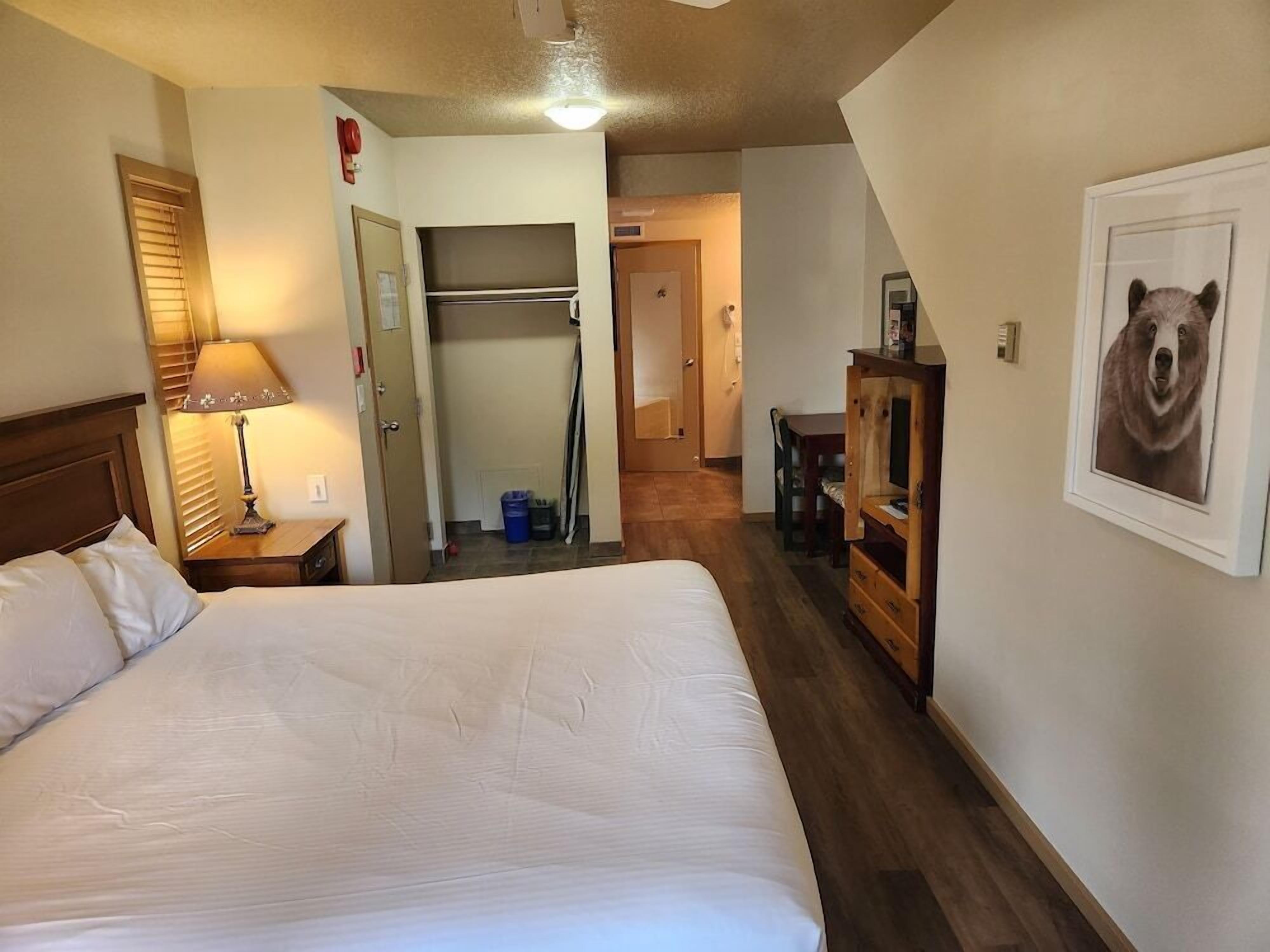 A hotel room with a large bed, a desk with a chair, a wardrobe, and a bear picture on the wall.