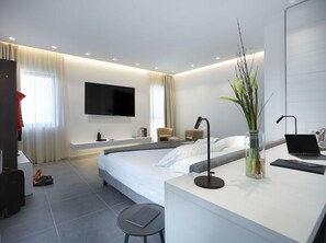 Habitación de hotel moderna con cama, escritorio con una computadora portátil, televisor de pantalla plana y un gran ventanal con cortinas.