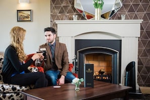 A man and a woman sitting on a sofa, holding drinks, with a fireplace and a framed picture in the background. - Shandon Hotel AND SPA (Portnablagh)