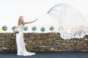 A person in a white dress standing in front of a stone wall with small flower arrangements.
