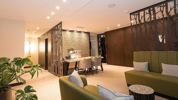 Ein modernes Wohnzimmer mit einem grünen Sofa, einem Essbereich mit Tisch und Stühlen und einer Wand mit einem Baumdekor.