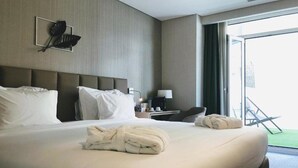 Ein Hotelzimmer mit einem großen Bett, einem Nachttisch, einer Lampe und Blick ins Freie.