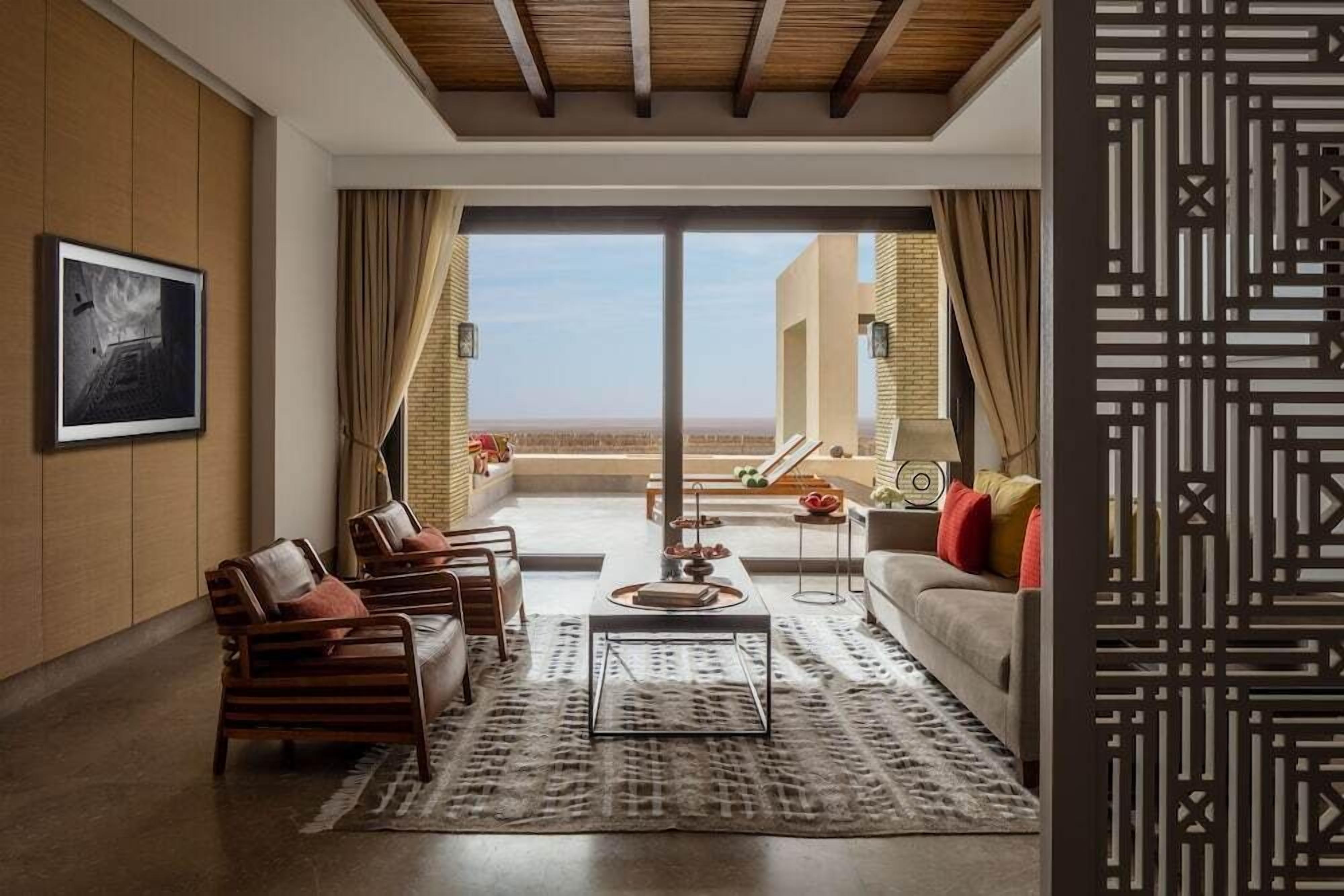Una sala de estar moderna con sofá, sillas, una mesa de centro y vistas al paisaje desértico a través de grandes ventanales.