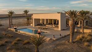 Un edificio moderno con piscina, asientos al aire libre y palmeras.