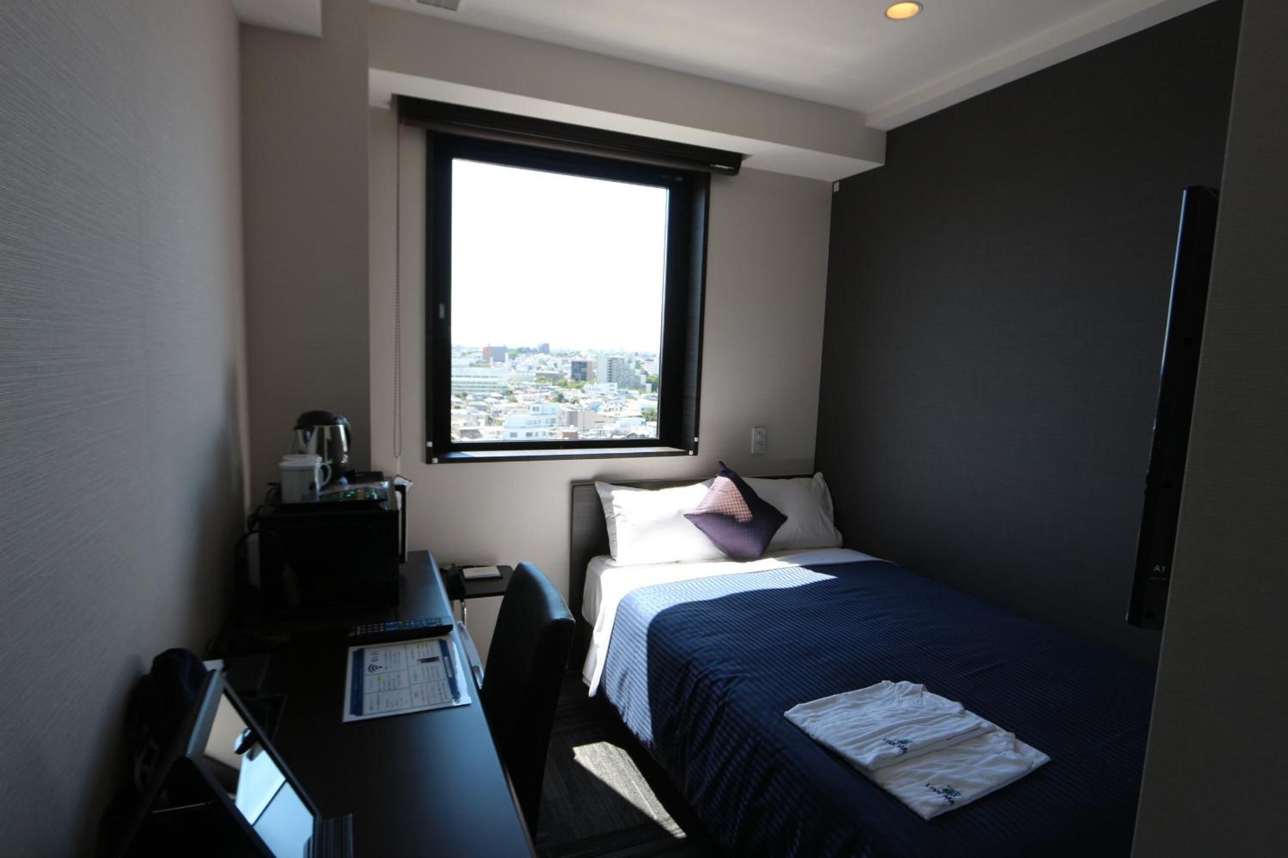 A hotel room with a bed, a desk, and a window with a city view.