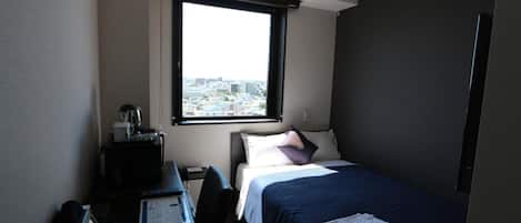 A hotel room with a bed, a desk, and a window with a city view.