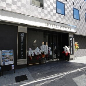 A hotel entrance with a checkered facade, a clear glass door, and white flowers displayed outside. - Hotel Livemax Takadanobaba Ekimae (Tokyo)