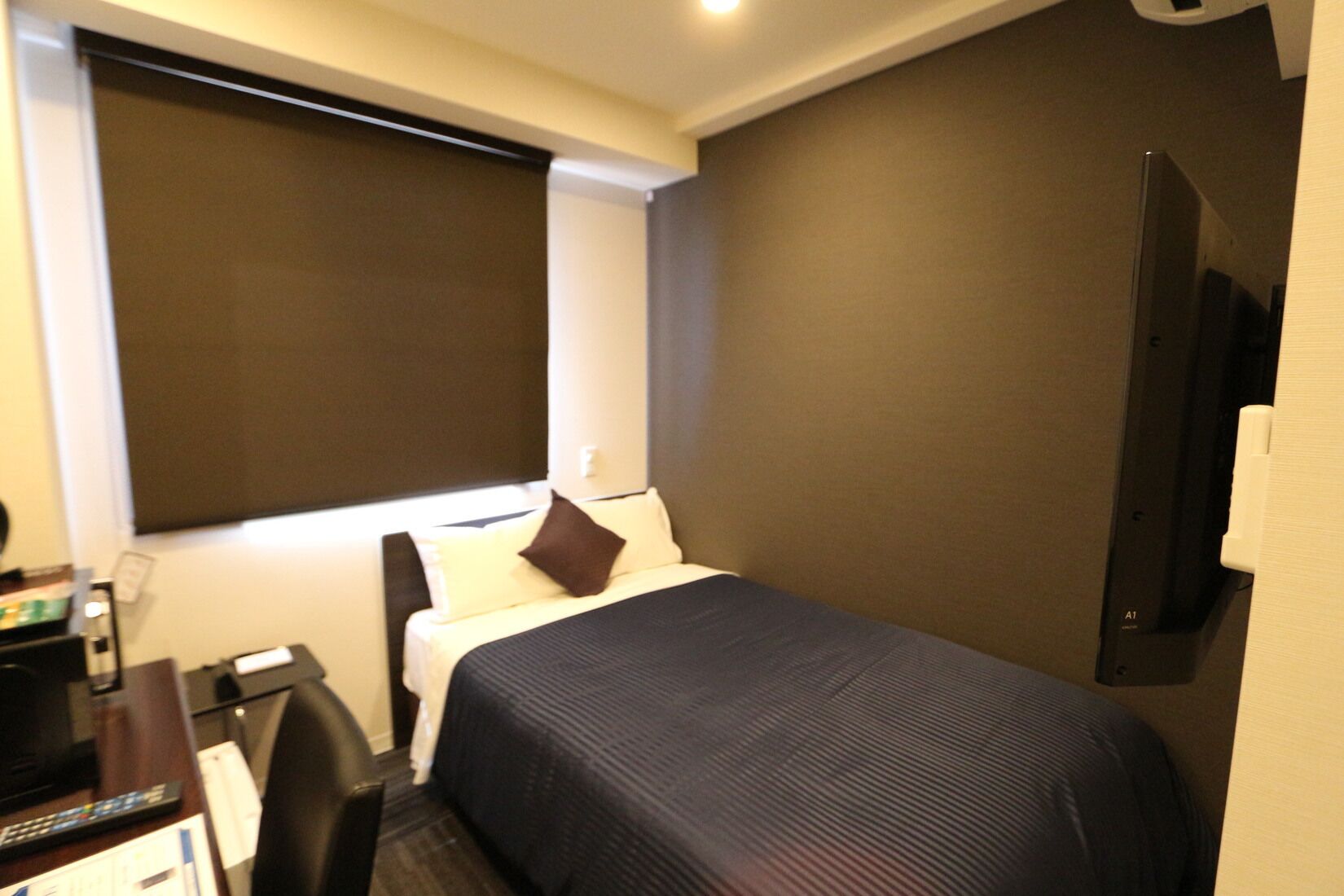 Una habitación de hotel con una cama, un escritorio con computadora, un televisor y una ventana con persiana.