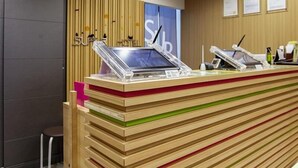 Ein Empfangstresen mit einer Uhr, eine Holzvertäfelung mit vertikalen Lamellen und eingeramte Aushänge an der Wand.