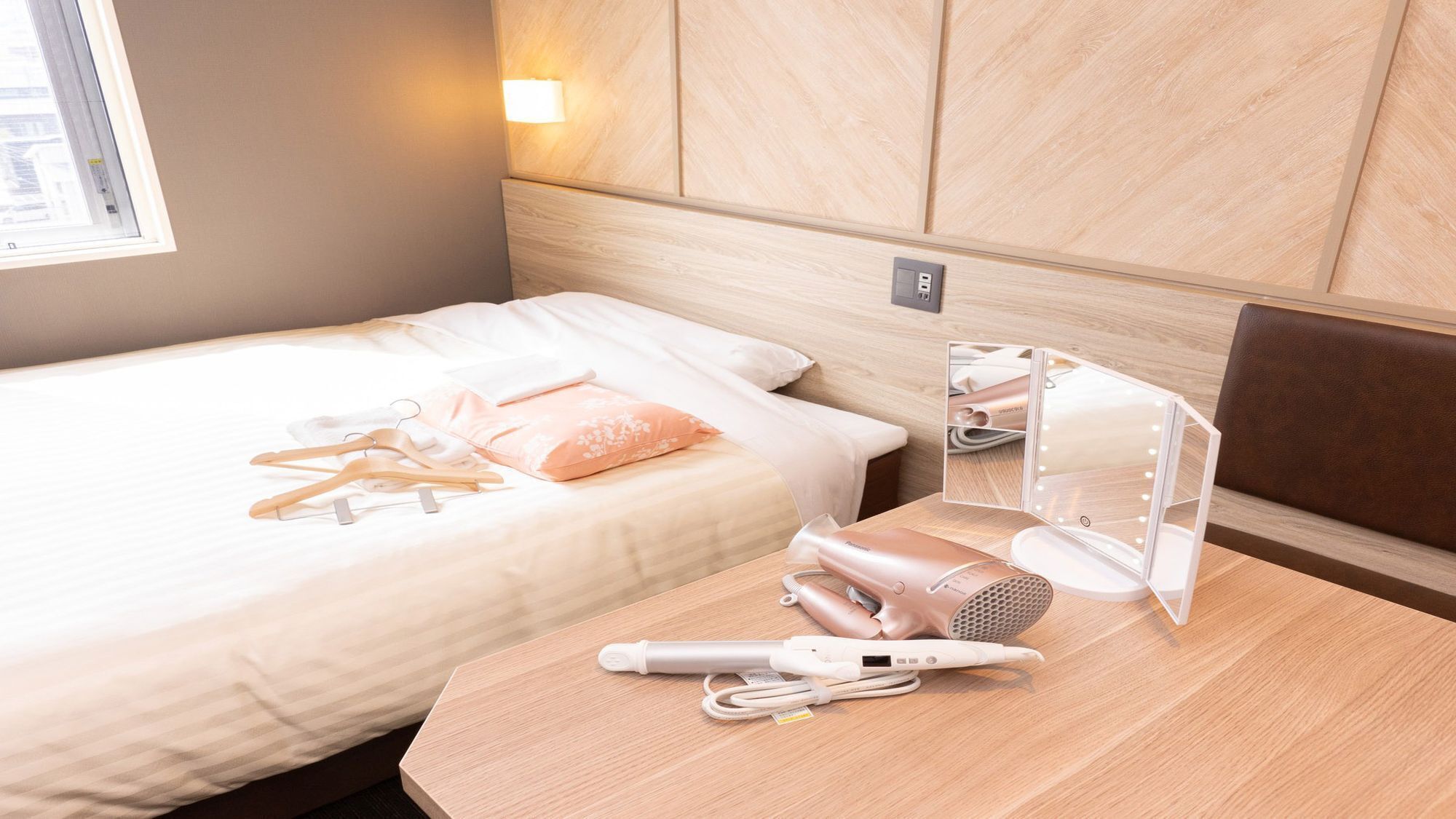 Ein Hotelzimmer mit Bett, Nachttisch mit Spiegel und Beleuchtung, Fön und einem mobilen Heizgerät.